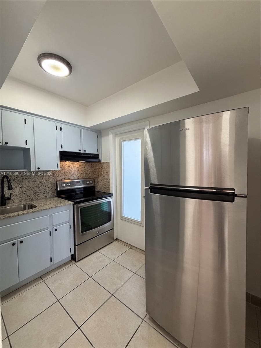 Kitchen featuring stainless steel appliances, stone-finish countertops, tiled flooring, built-in cabinetry, and a flush-mount ceiling light