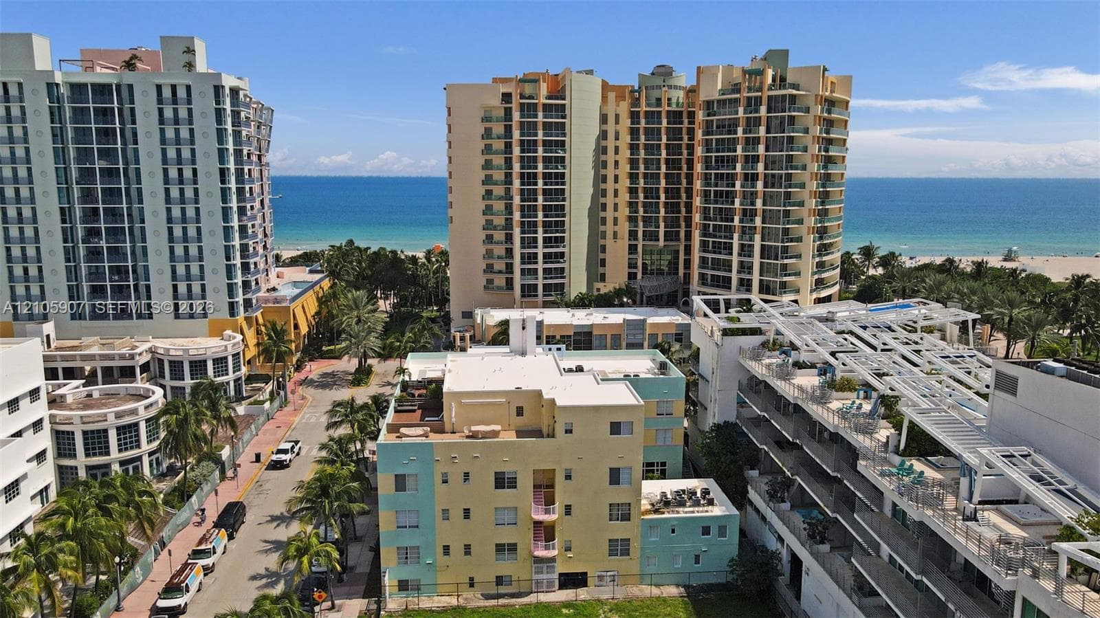 Aerial perspective of a multi-story coastal development featuring direct ocean frontage, high-rise architectural structures, expansive sandy coastline, and established tropical landscaping