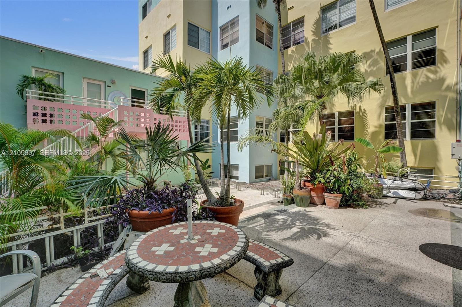 Exterior courtyard featuring a concrete patio, pastel-toned building facade, integrated staircase with decorative breeze block railing, and mature palm trees