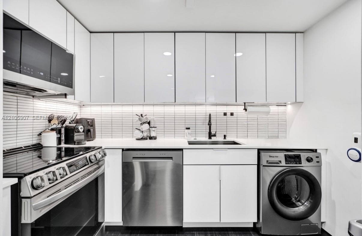 Sleek kitchen featuring high-gloss white cabinetry, linear tiled backsplash, integrated stainless steel appliances, solid surface countertops, and under-cabinet lighting