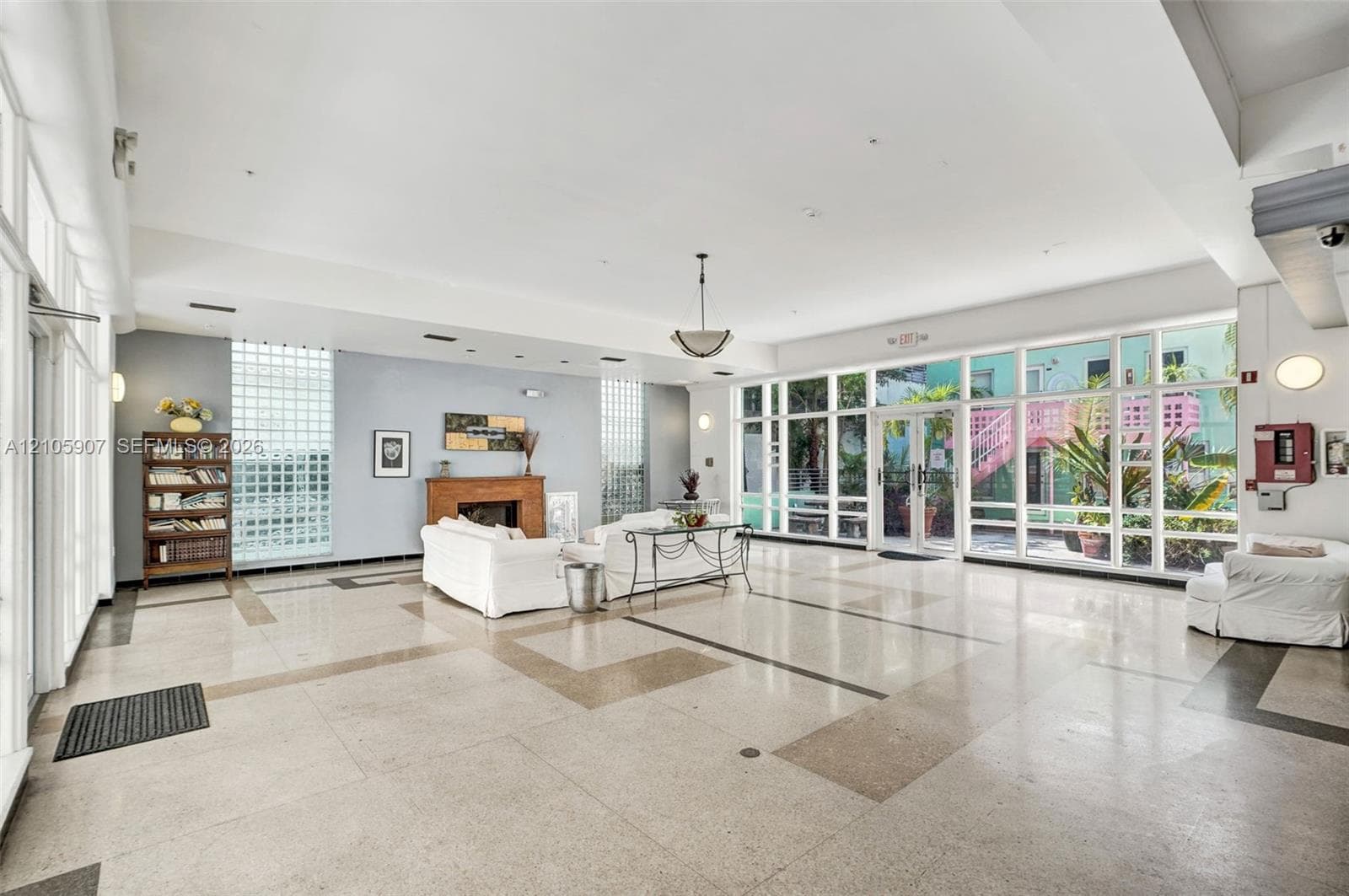 Expansive open-concept room featuring high ceilings, polished stone flooring with geometric inlay, floor-to-ceiling glass panel walls, dual glass block windows, and a built-in wood-finished fireplace