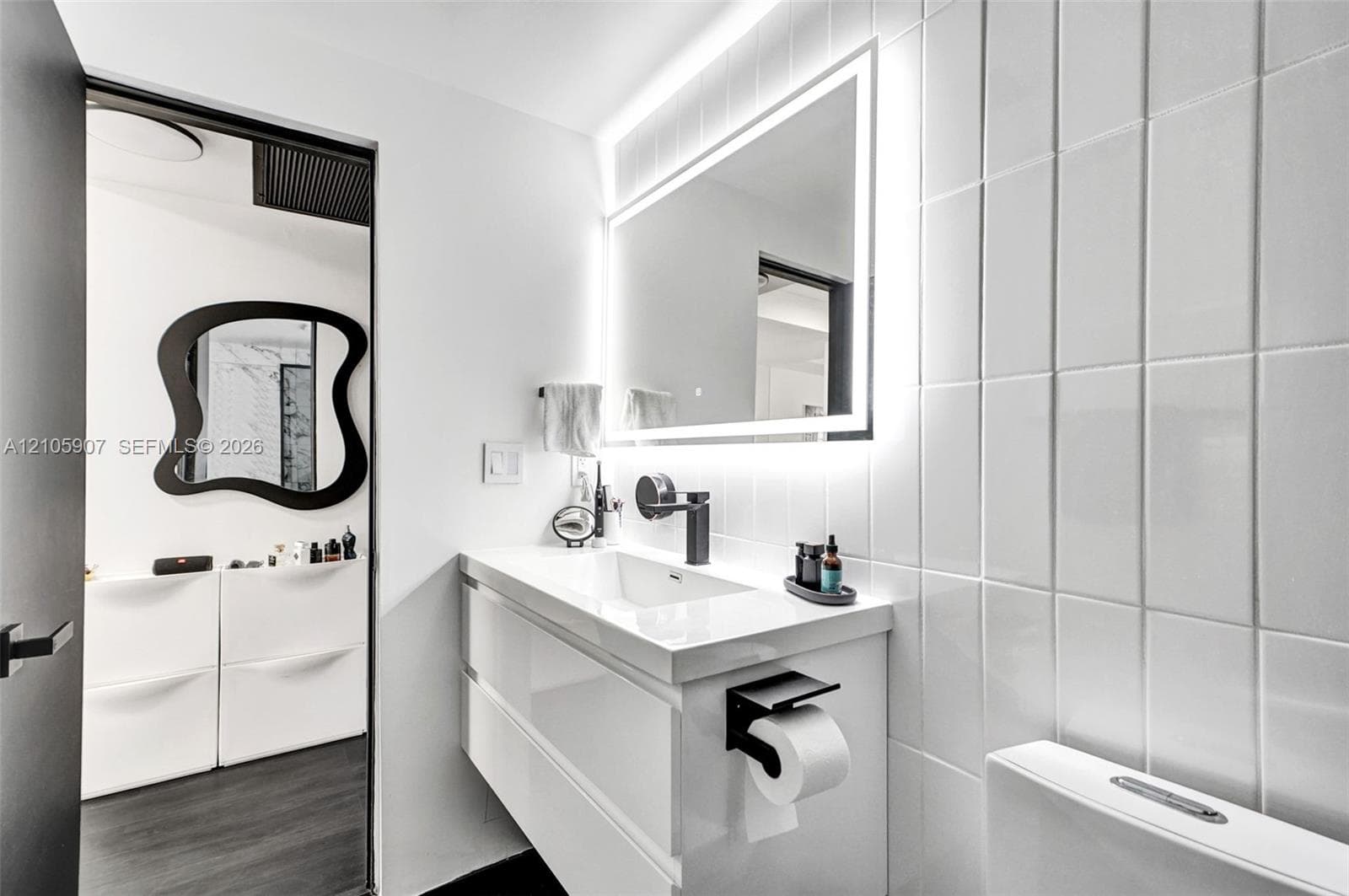 Wall-mounted floating vanity with integrated rectangular sink, matte black wall-mounted faucet, rectangular LED-backlit mirror, and vertical glossy white wall tile