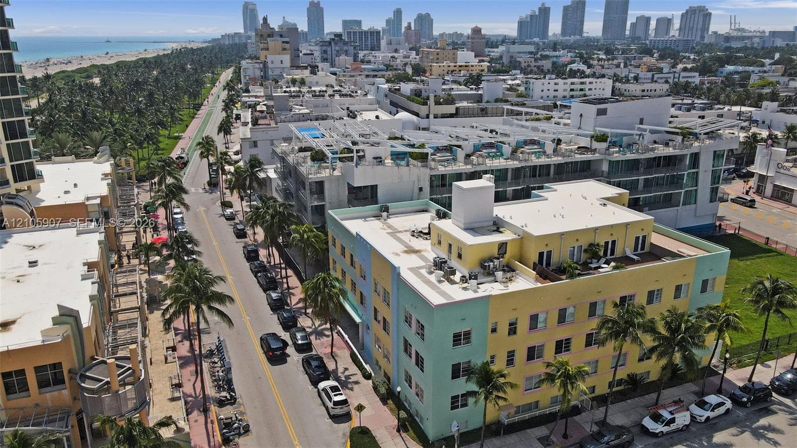 Aerial perspective of a multi-story building featuring a flat roof with rooftop terraces, light-colored facade, and proximity to the coastline and metropolitan skyline