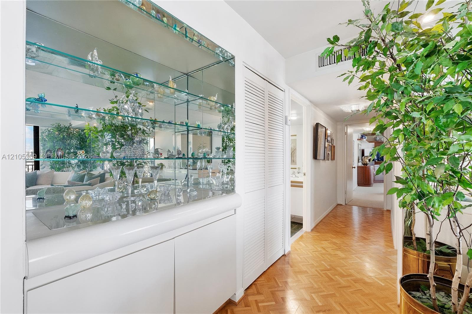 Built-in cabinetry featuring mirrored backing and glass shelving, white louvered closet doors, and herringbone-patterned wood flooring