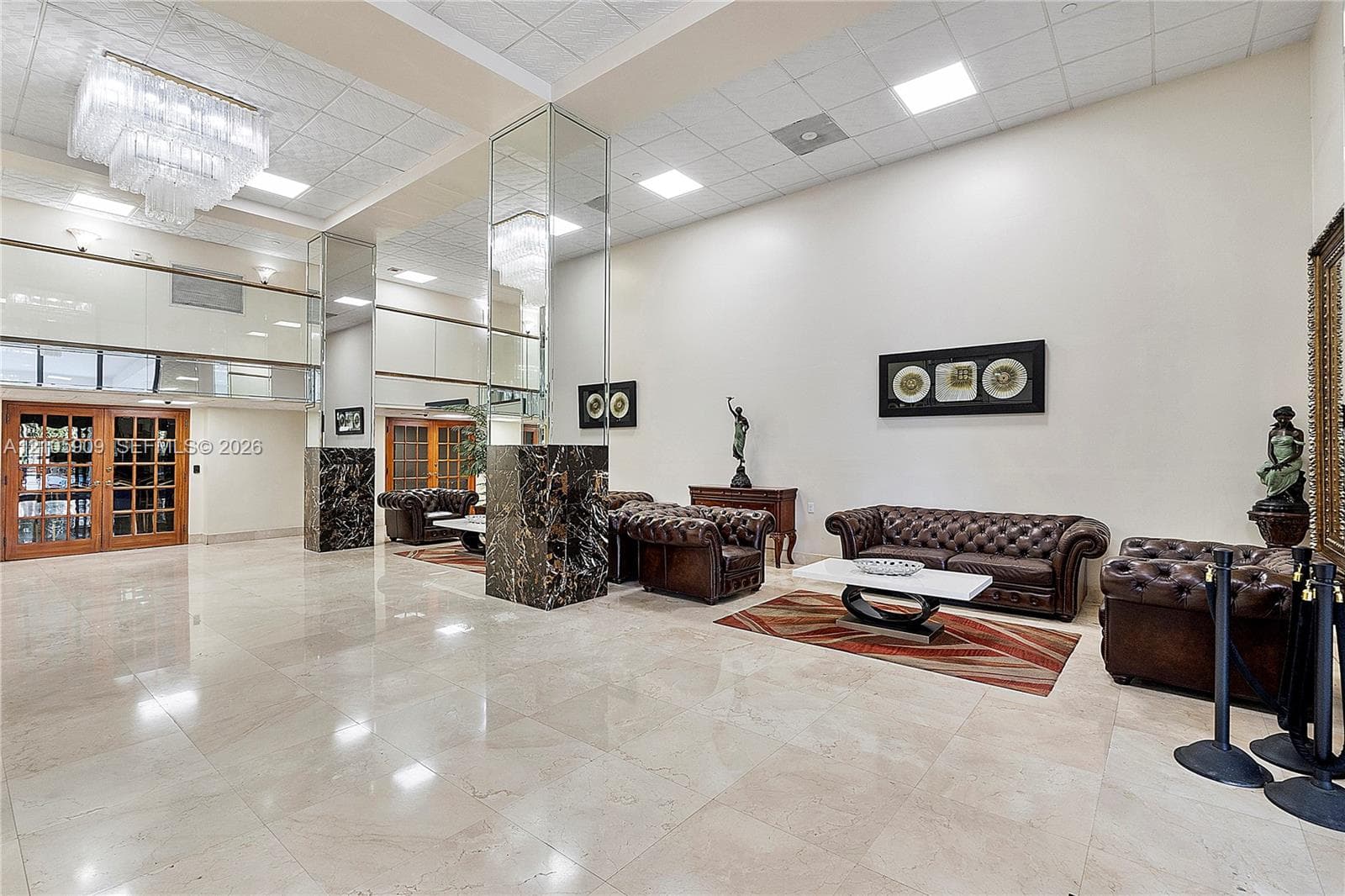 Expansive lobby featuring polished stone flooring, high ceilings with recessed lighting, tiered crystal chandelier, and mirrored support columns with dark stone bases