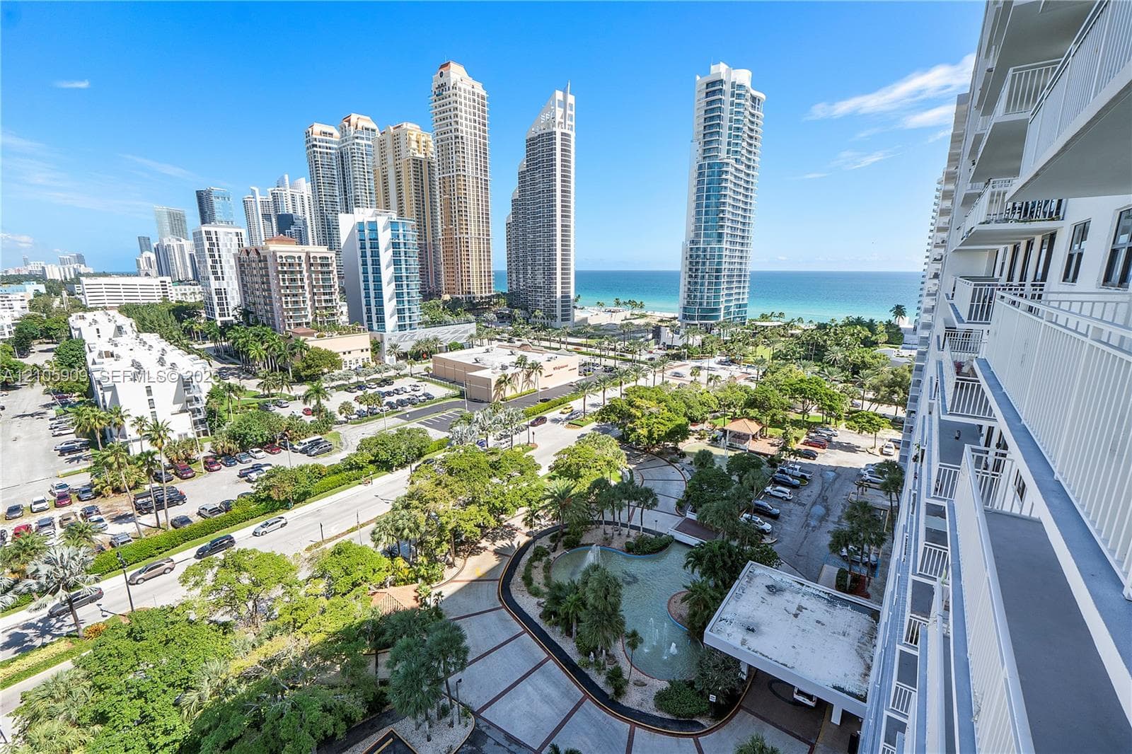 Elevated balcony offering an expansive cityscape and ocean horizon, overlooking a landscaped courtyard with a decorative fountain and pedestrian pathways