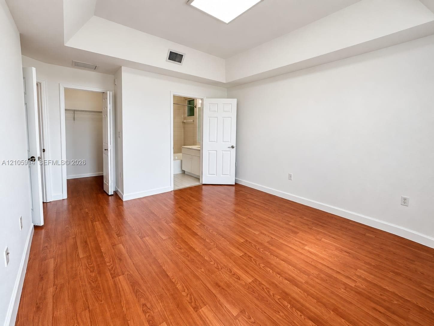 Room featuring wood-finish flooring, a tray ceiling, recessed lighting, and dual entry points to a walk-in closet and an en-suite bathroom