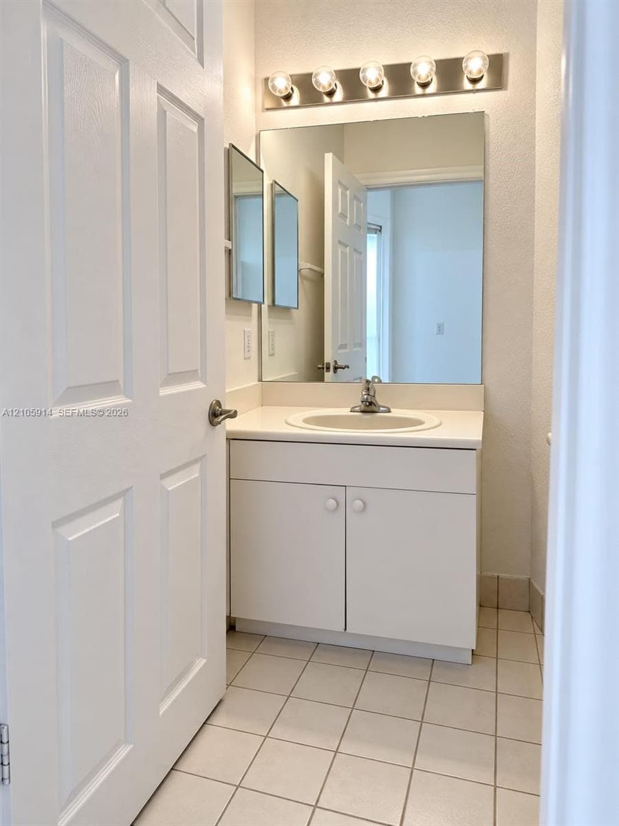 Vanity cabinet with a white countertop and integrated sink, wall-mounted mirror, five-light fixture, and ceramic tile flooring