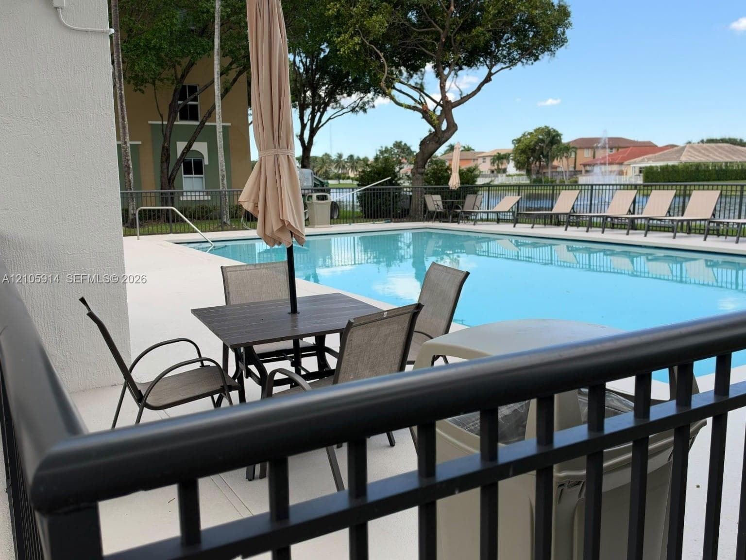 In-ground swimming pool with light-colored concrete decking, metal perimeter fencing, and water feature