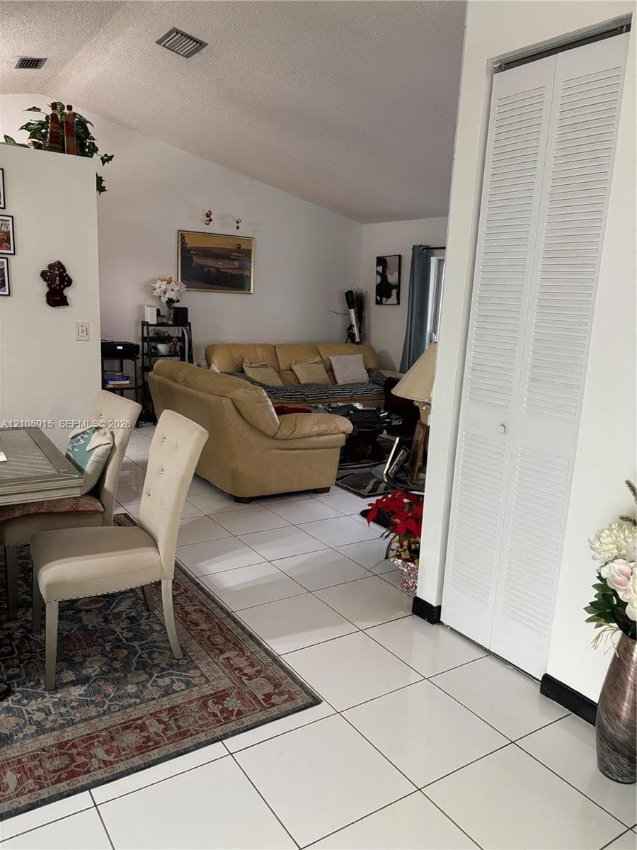 Open-concept interior featuring vaulted ceilings, neutral ceramic tile flooring, and floor-to-ceiling bi-fold closet doors