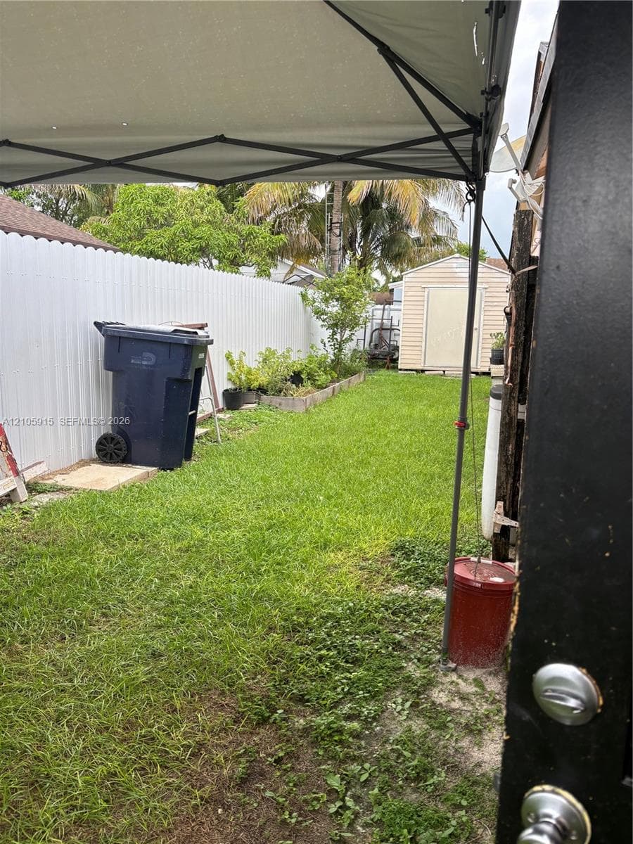 Backyard featuring a grass lawn, white vinyl privacy fencing, raised garden beds, and a detached storage shed