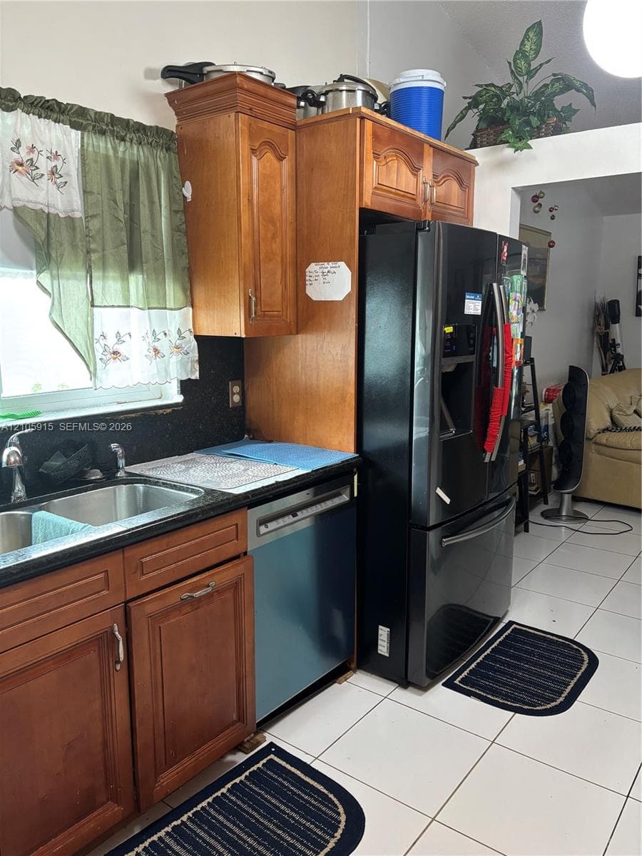 Kitchen featuring wood cabinetry, dark countertops, integrated stainless steel double-basin sink, and ceramic tile flooring