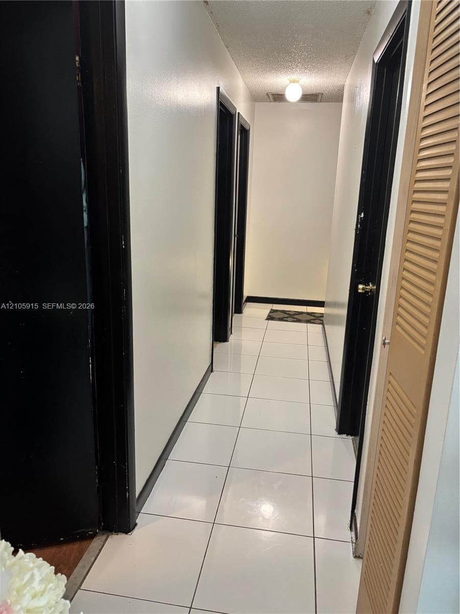 Hallway featuring high-gloss white floor tiling, contrasting black door frames, and a built-in louvered closet door
