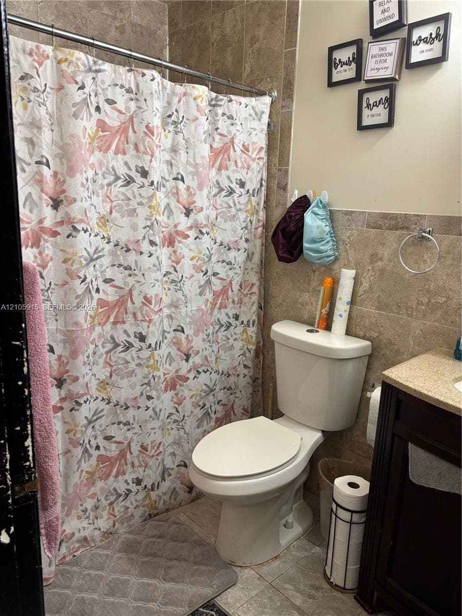 Bathroom featuring a tub-shower combination with full-height stone-finish wall tile, dark-finish wood cabinetry, and a stone-finish vanity countertop