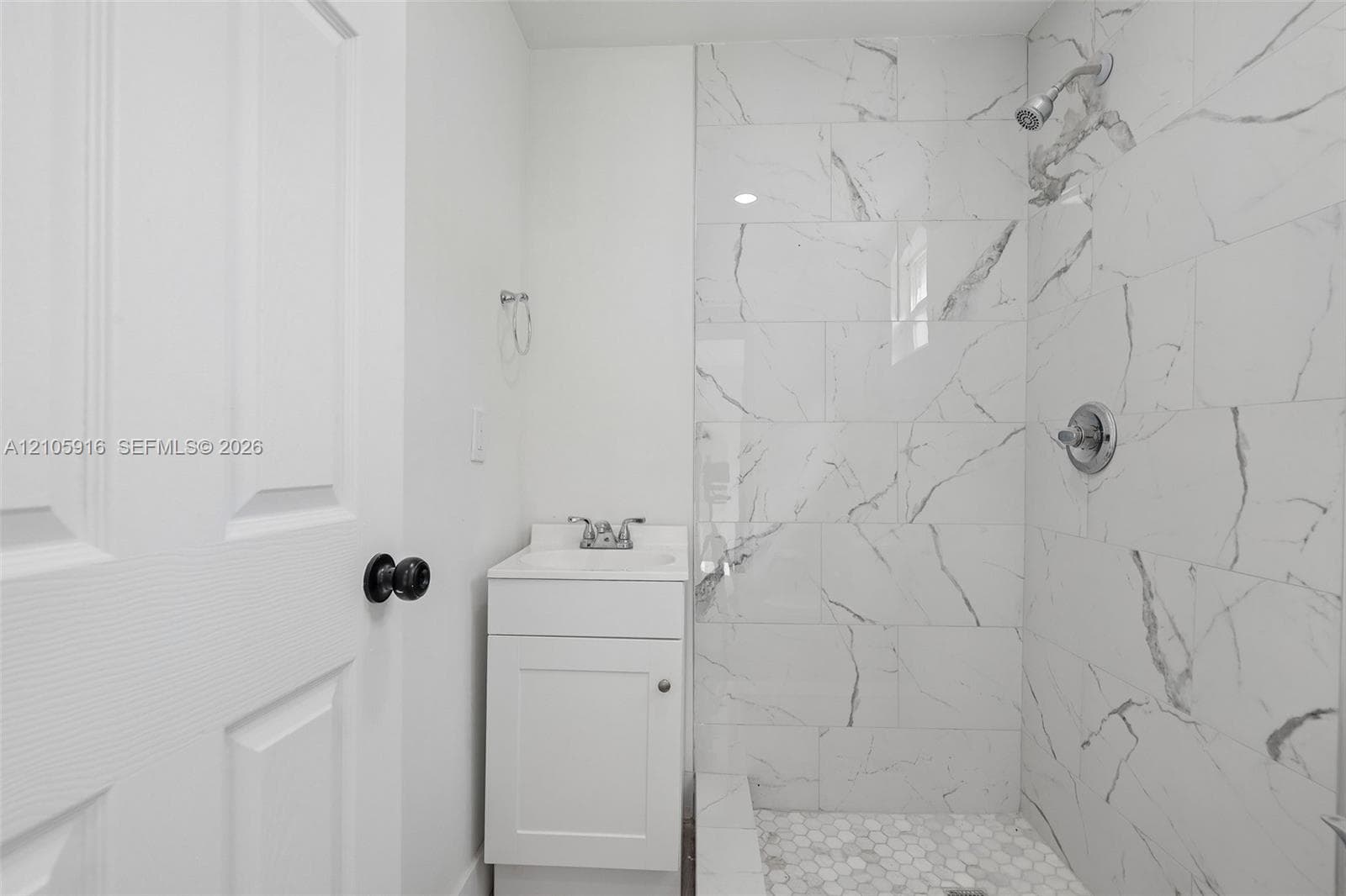 Bathroom featuring a white vanity cabinet, rectangular sink, shower enclosure with large-format veined tile surround, and hexagonal tile shower flooring