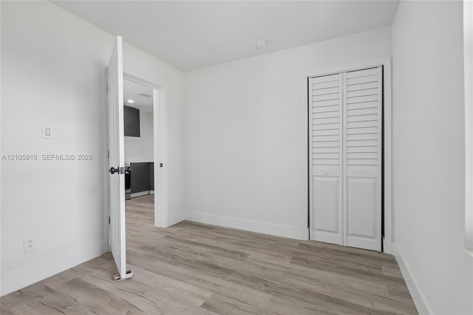 Neutral interior space featuring wood-finish flooring, white walls, and a closet with white louvered bifold doors