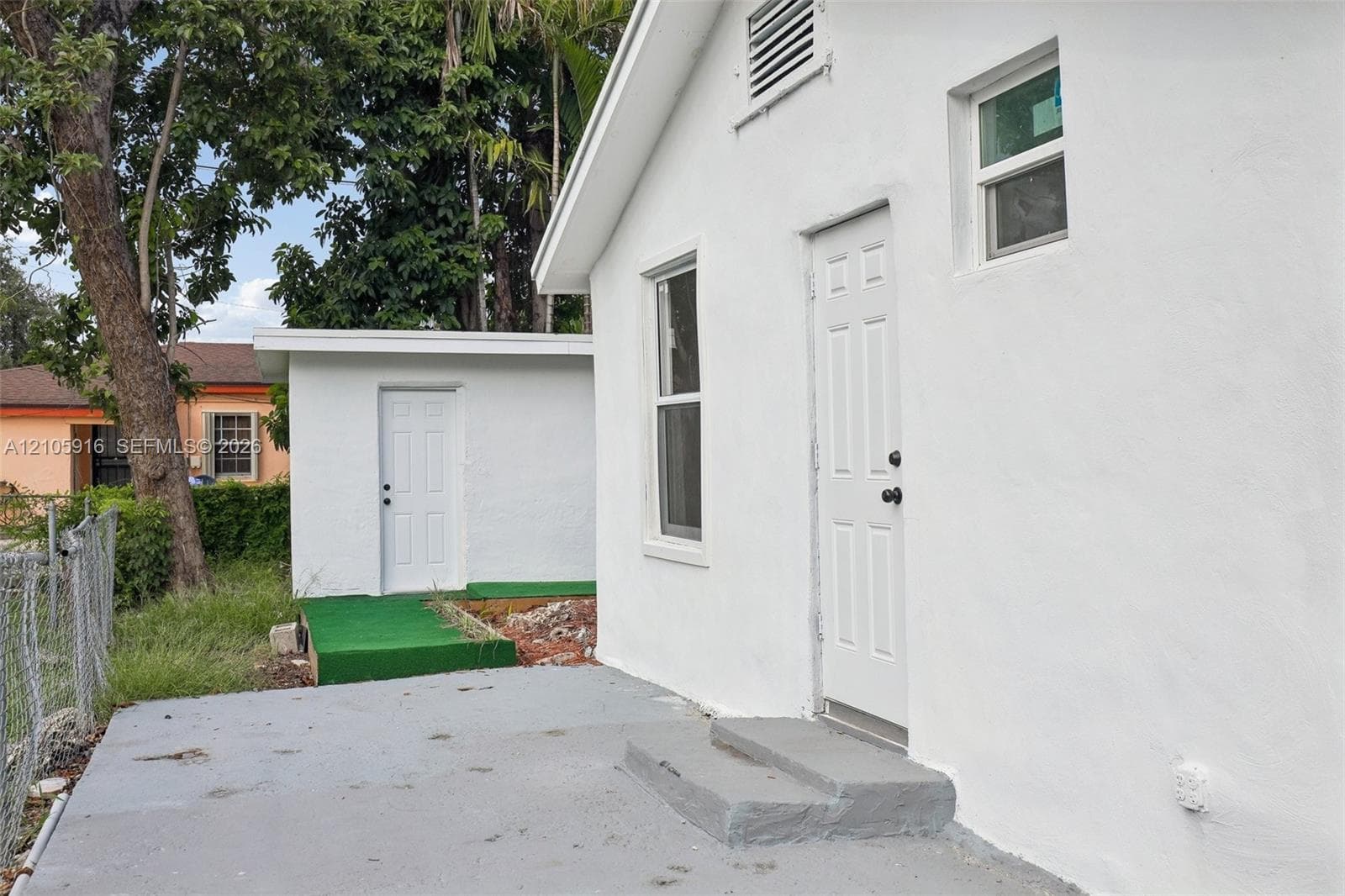 Exterior featuring white stucco siding, dual entry doors, concrete patio, and a separate detached structure