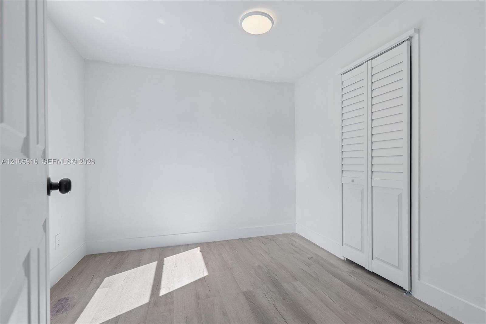 Room featuring wood-finish flooring, white walls, louvered bi-fold closet doors, and a flush-mount ceiling light fixture