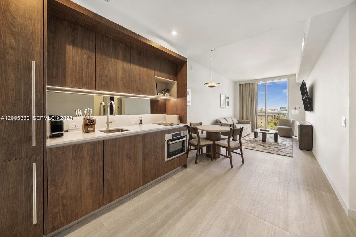 Kitchen featuring wood-finish cabinetry, a mirrored backsplash, built-in oven, solid surface countertop with integrated sink, and wood-finish flooring