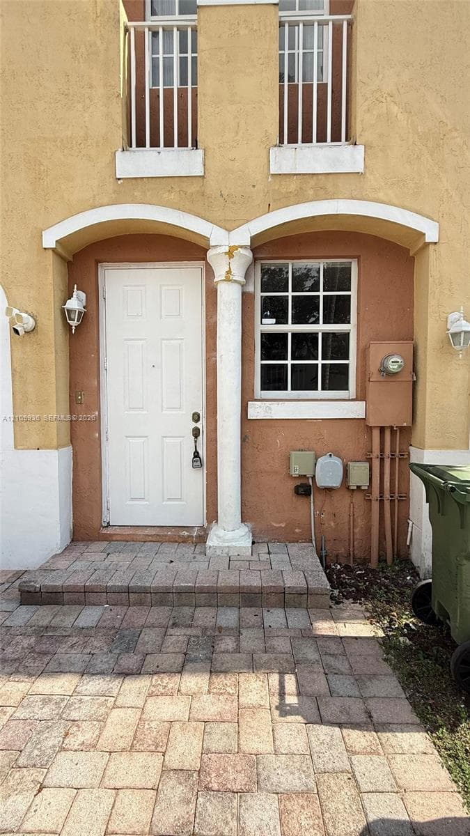 Stucco exterior featuring dual arched entryways, a central decorative column, grid-patterned windows, and paver-stone entry flooring