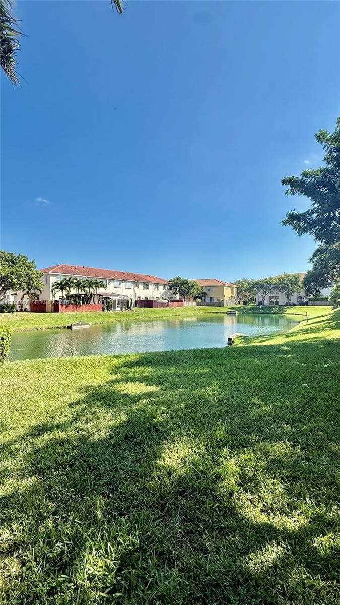 Waterfront setting featuring a central pond, expansive lawn, mature palm trees, and terracotta-tiled roof architecture