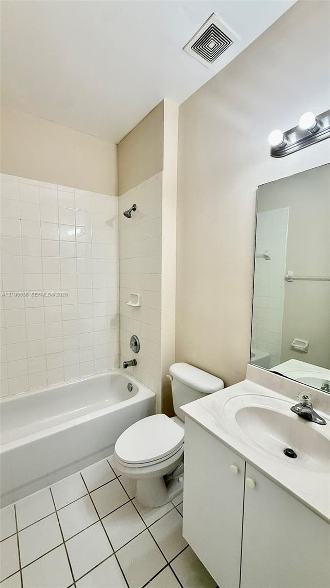 Bathroom featuring a white vanity cabinet with an integrated sink, wall-mounted mirror, ceramic tile flooring, and a shower-tub combination with white tile surround