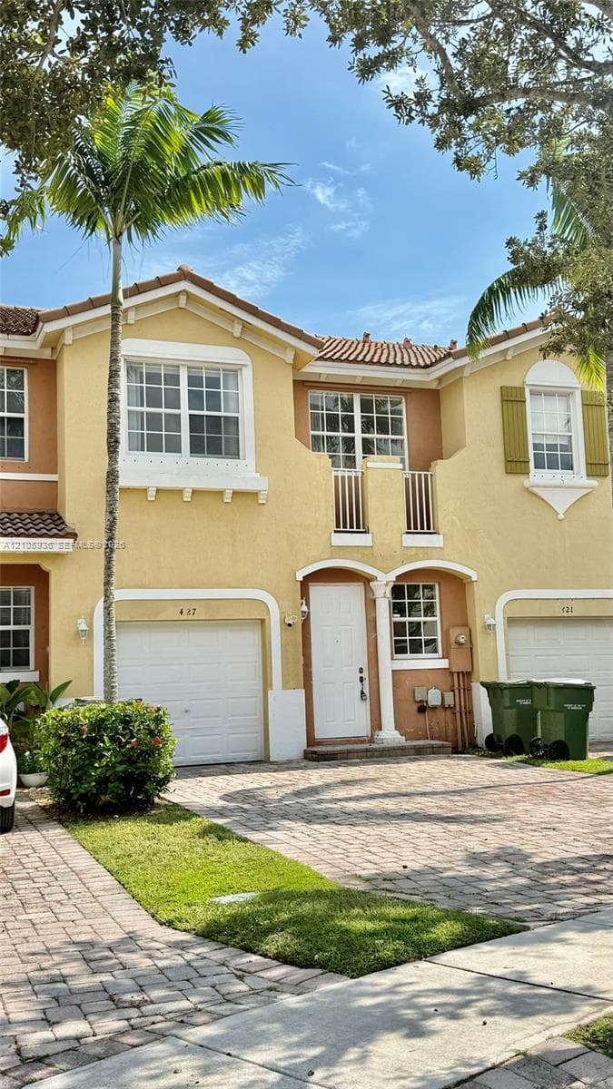 Two-story exterior featuring stucco siding, a tiled roof, a private second-story balcony with railings, and a paved driveway