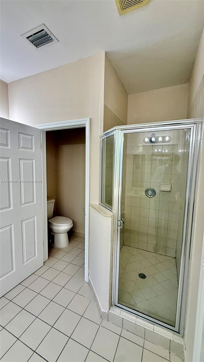 Corner glass-enclosed shower with tiled surround, porcelain tile flooring, and separate water closet