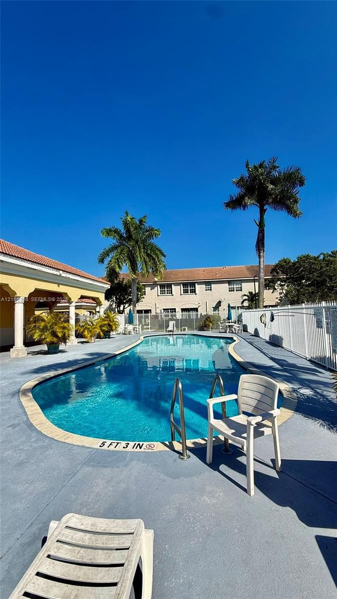 In-ground swimming pool with a concrete deck, metal perimeter fencing, and mature palm trees