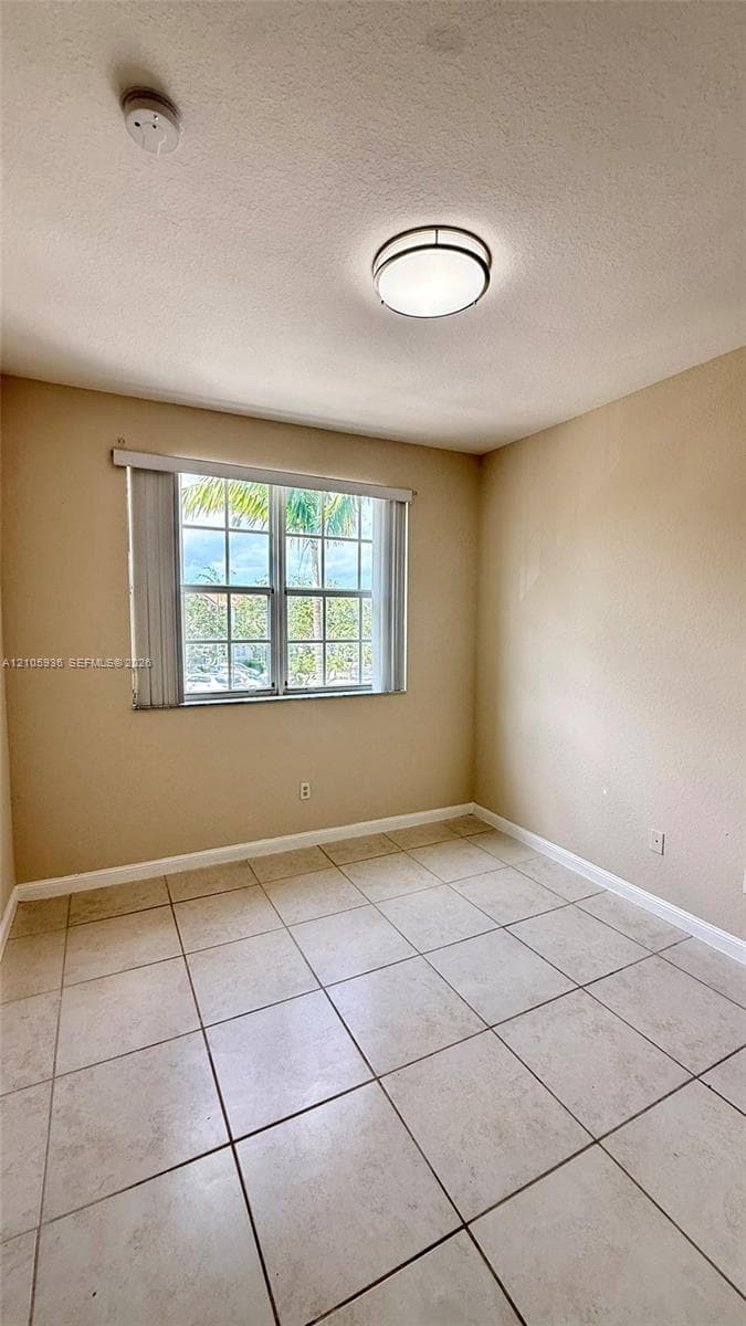 Room featuring neutral wall tones, large-format tile flooring, a multi-pane window with vertical blinds, and a round flush-mount ceiling fixture