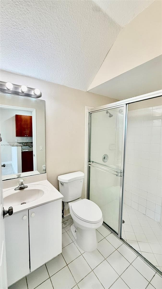 Bathroom featuring a single-sink vanity with white cabinetry, a glass-enclosed shower with tiled walls, ceramic floor tiling, and wall-mounted light fixtures above the mirror