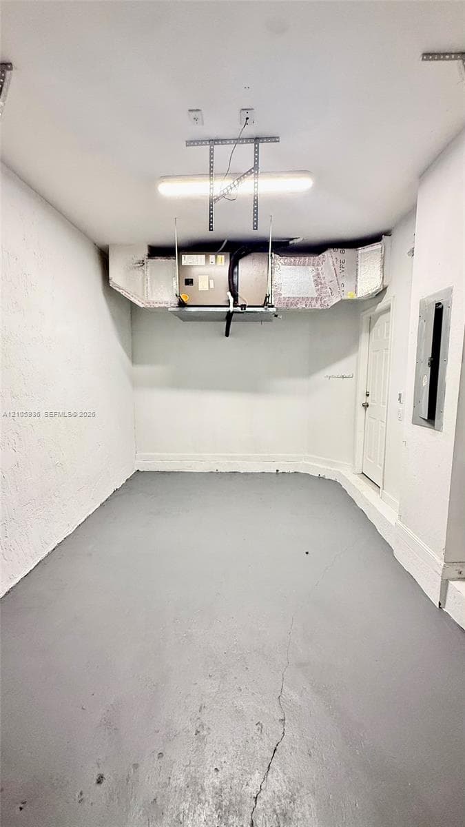 Enclosed storage space featuring painted concrete flooring, wall-mounted electrical panel, ceiling-mounted fluorescent lighting, and overhead HVAC system