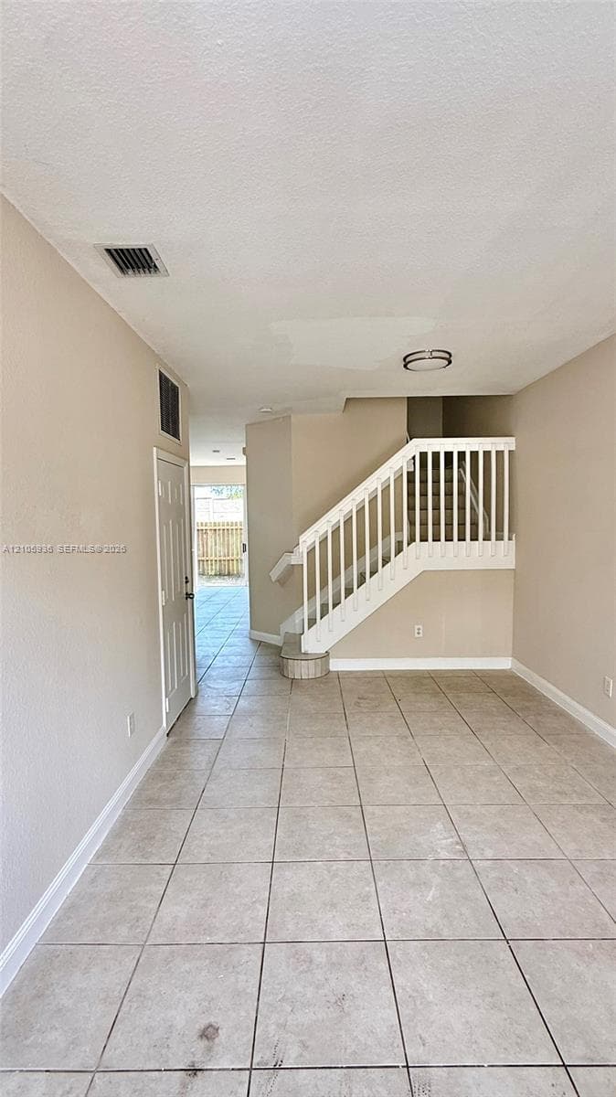 Interior space featuring neutral wall tones, large-format tile flooring, a white-railed staircase, and a flush-mount ceiling light fixture