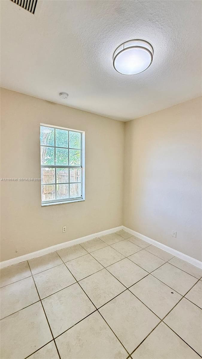 Room featuring neutral-toned tile flooring, light-colored walls, a single-pane window with grid detailing, and a circular flush-mount ceiling light fixture