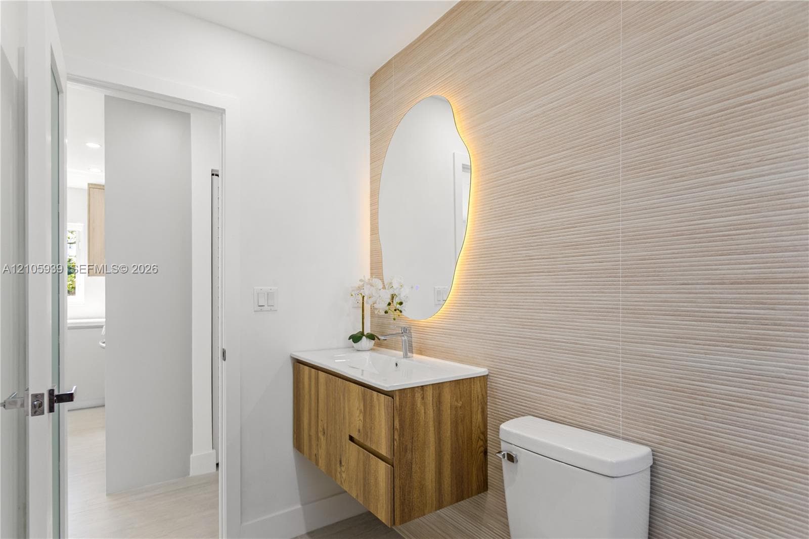 Floating wood-finish vanity with an integrated sink, organic-shaped backlit mirror, and textured tile wall accent