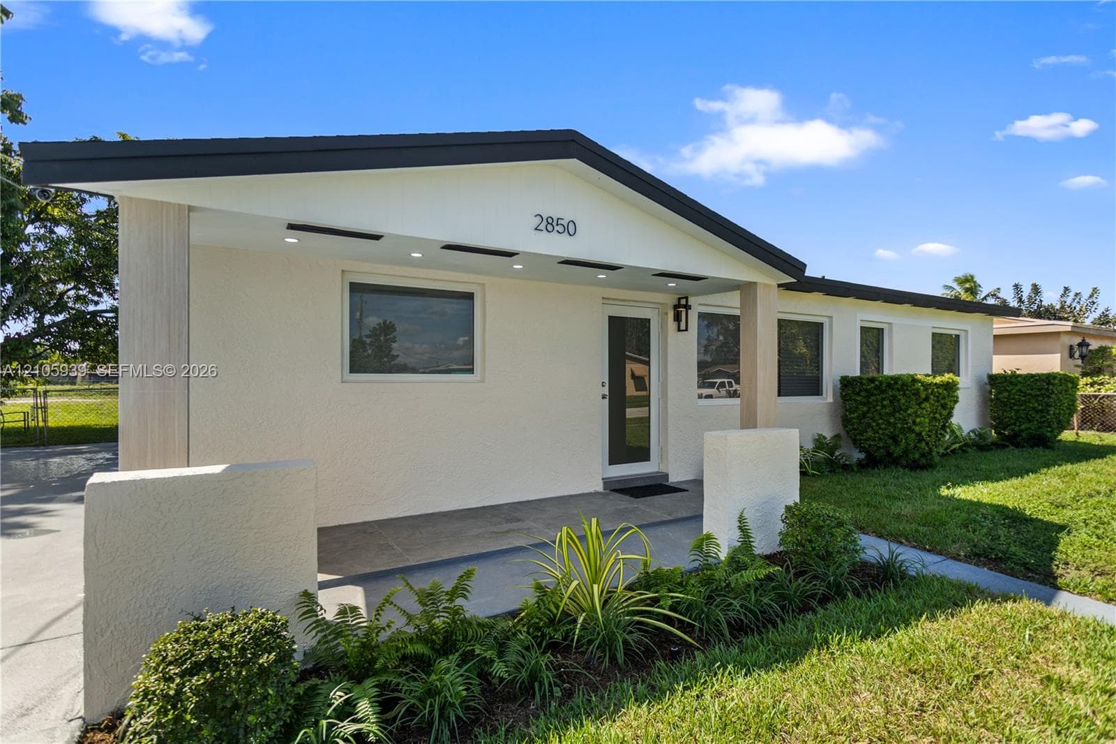 Single-story exterior featuring a textured stucco facade, covered porch with recessed lighting, and architectural gable roofline