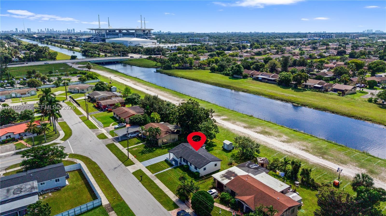 Aerial perspective of a detached single-story residence situated along a canal-front lot, featuring a shingled roof, concrete driveway, and established lawn