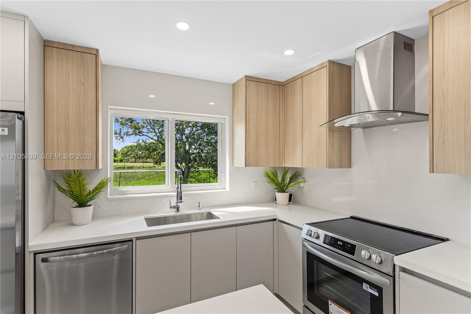 Kitchen featuring light wood-finish cabinetry, stainless steel appliances, solid-surface countertops, a stainless steel undermount sink, and an integrated stainless steel range hood
