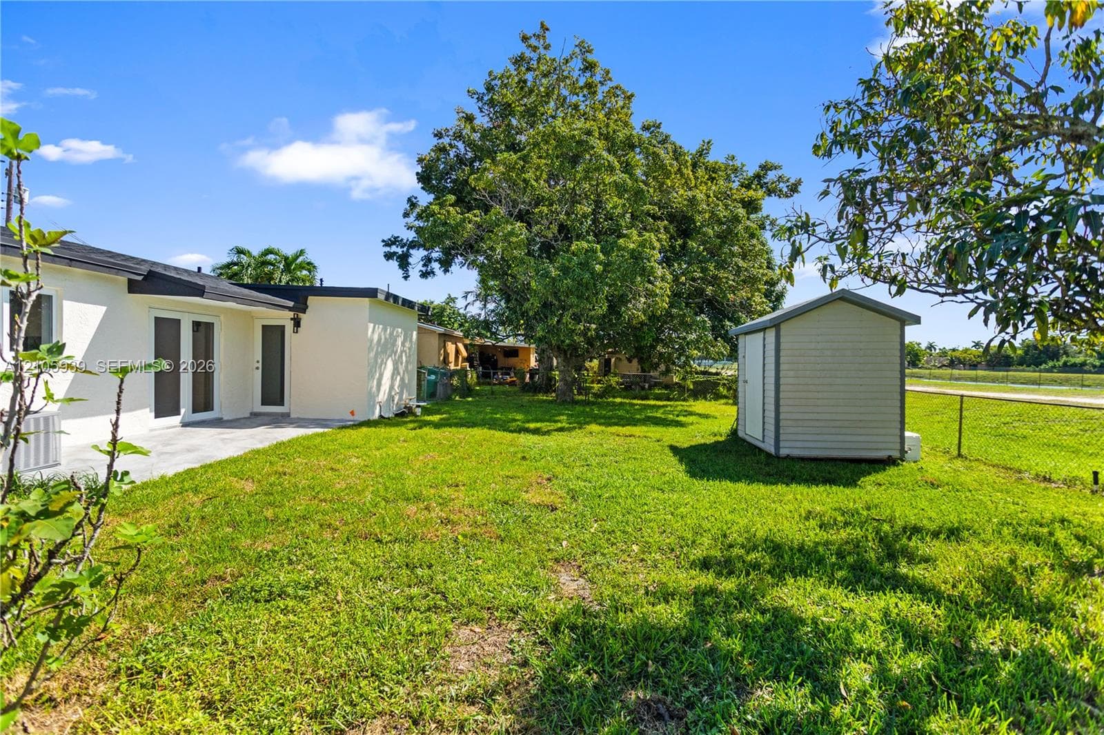 Backyard featuring a concrete patio, freestanding storage shed, established trees, and chain-link fencing