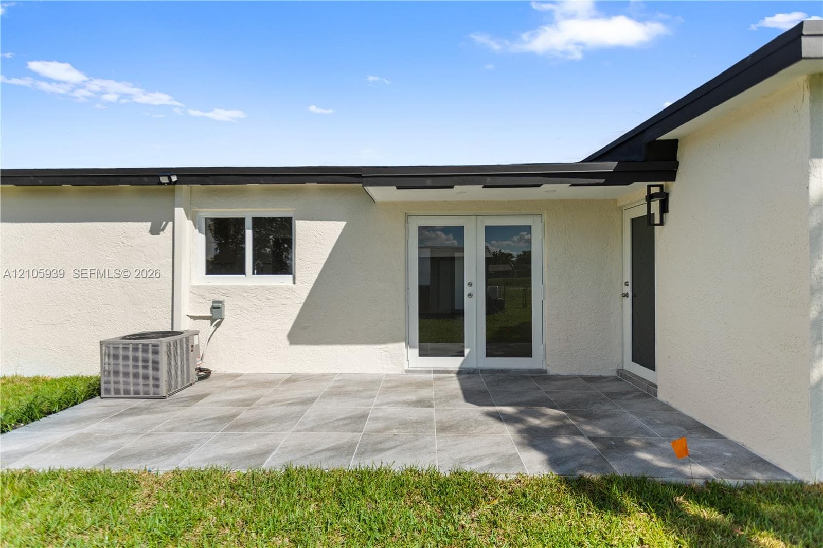 Rear patio featuring large-format gray tile flooring, double-glass entry doors, an attached exterior light fixture, and a stucco finish