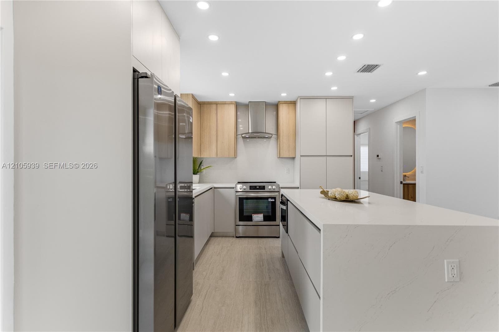 Kitchen featuring a waterfall-edge stone island, stainless steel appliances, a modern stainless steel range hood, dual-tone cabinetry, and wood-finish flooring