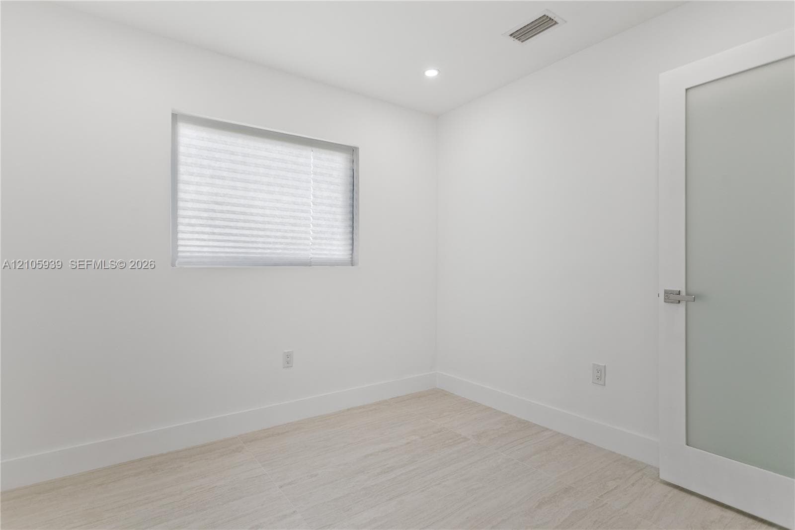 Neutral interior space featuring wood-finish flooring, recessed lighting, and a frosted glass-panel door