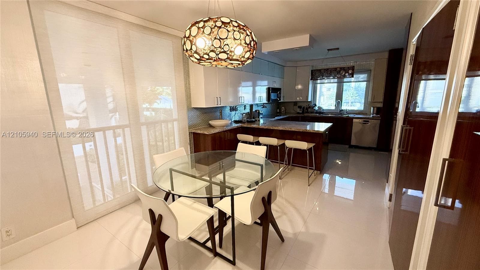 Kitchen area featuring high-gloss cabinetry, stone countertops, a multi-level breakfast bar, large-format tile flooring, and a decorative orb-style pendant light fixture