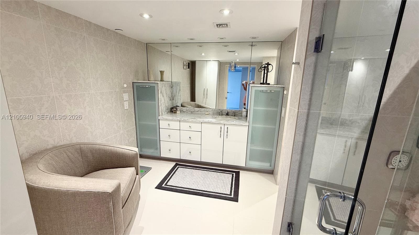 Built-in vanity featuring high-gloss cabinetry, stone countertops, integrated side storage towers with glass-panel doors, and a full-width wall mirror