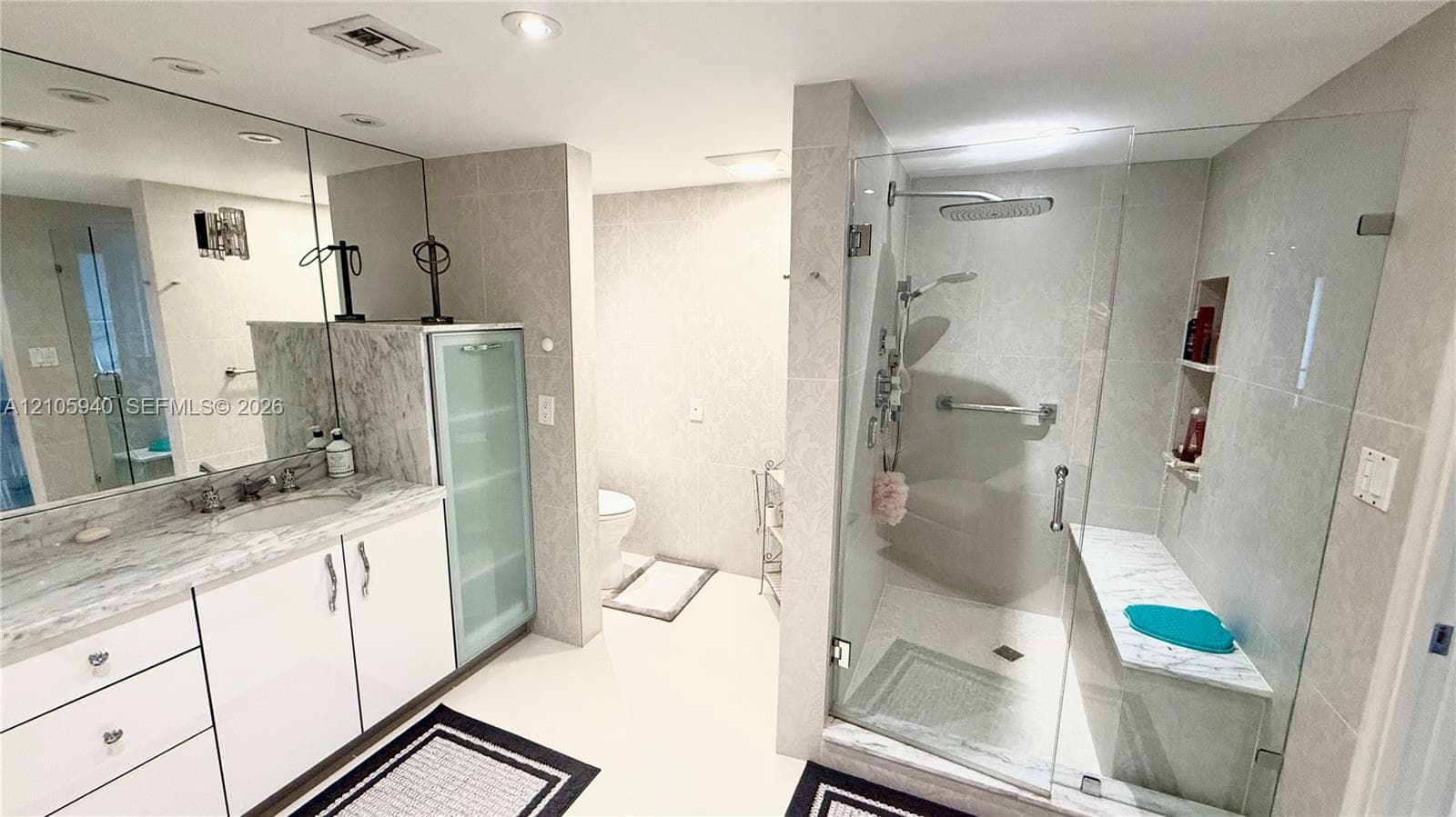 Bathroom featuring a vanity with stone countertop, integrated cabinetry with glass-front storage, recessed lighting, and a frameless glass-enclosed shower with a built-in stone bench
