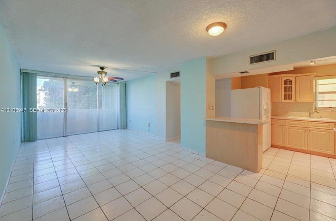 Open-concept interior featuring light-toned tile flooring, large sliding glass doors, built-in breakfast bar, cabinetry with glass-paneled accents, and recessed ceiling lighting