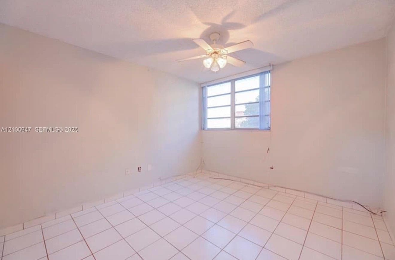 Interior space featuring large-format tile flooring, multi-pane window with vertical blinds, and a ceiling-mounted light fixture with a five-blade fan