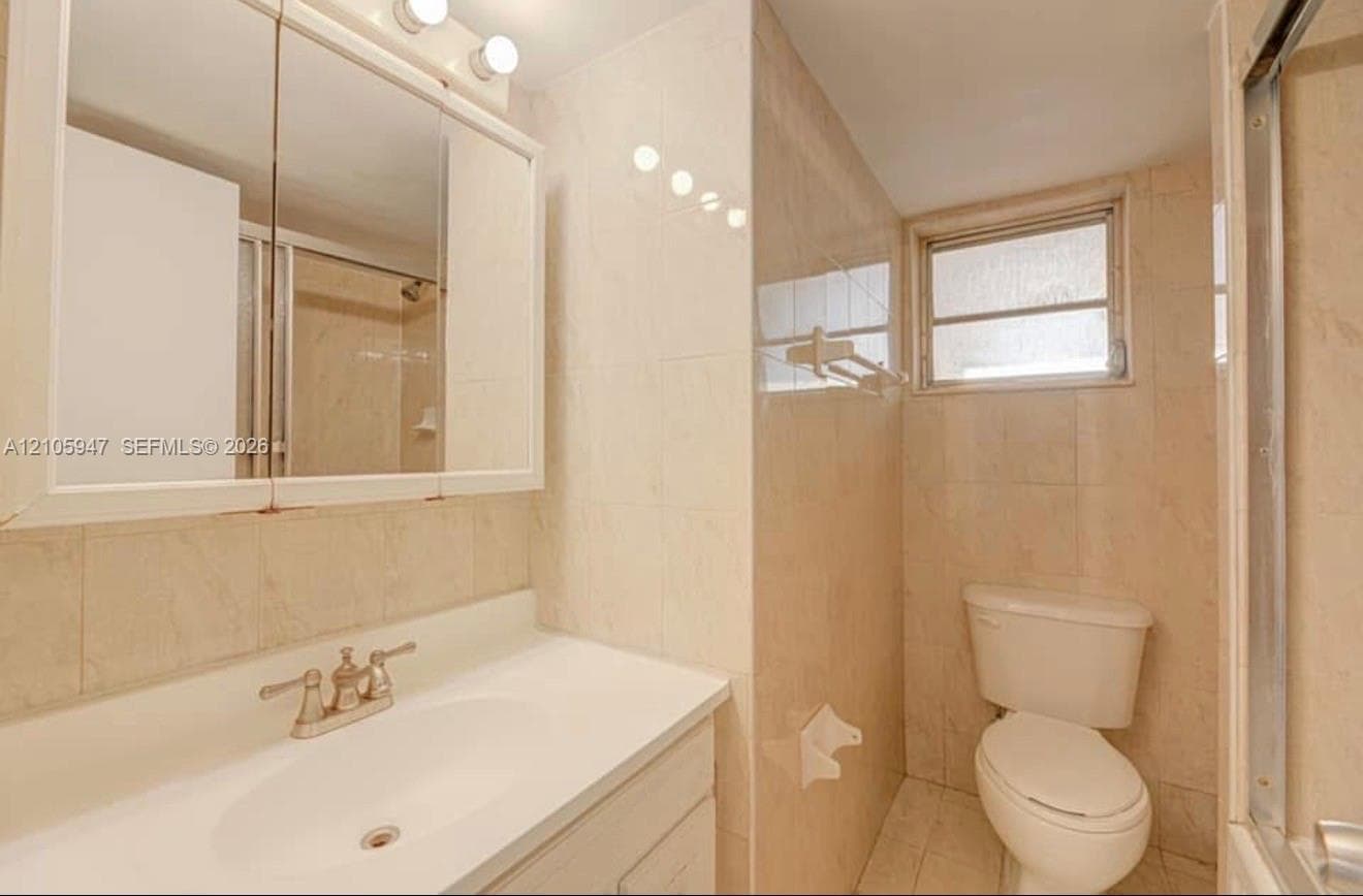 Bathroom featuring floor-to-ceiling tile, integrated vanity with a basin sink, tri-fold medicine cabinet, and a framed shower enclosure