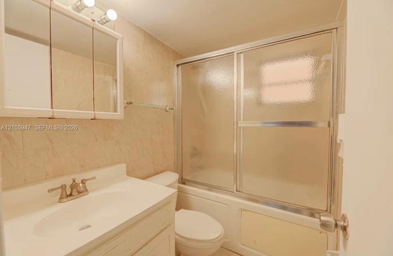 Full bathroom featuring a vanity with an integrated sink, tri-panel medicine cabinet, tiled wall surround, and a tub-shower combination with sliding glass doors