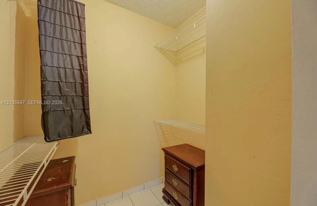 Walk-in storage space featuring white wire shelving and tile flooring